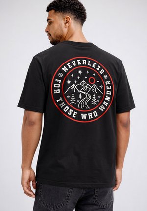 Man wearing black T-shirt with circular mountain, trees, stars, and sun design, text reads "Nevertheless For Those Who Wander."