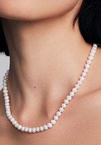 Białe perlówki z różnymi rozmiarami gładkich, lśniących pereł, nawleczone razem, tworząc delikatny, okrągły wzór.