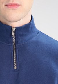 Navy blue zip-up sweatshirt with a high collar, featuring a silver zipper and a smooth, soft texture.
