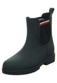 Stivaletto alla caviglia in gomma nera con pannelli laterali elastici caratterizzati da strisce rosse e bianche. Suola piatta con grip testurizzato, esterno liscio, punta arrotondata.