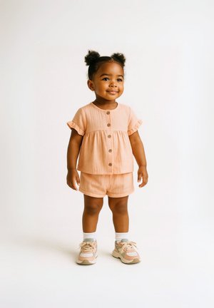 Ensemble en lin pêche comprenant un haut à volants et un pantalon court avec un bouton à l'avant. Associé à des baskets grises et roses et des chaussettes blanches. Texture lisse, coupe décontractée.