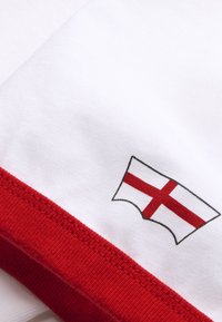 Λευκό ύφασμα με κόκκινη επένδυση που διαθέτει ένα μικρό έμβλημα της σημαίας της Αγγλίας με μαύρο περίγραμμα κοντά στην άκρη.