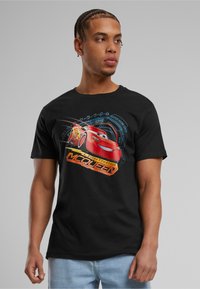 Sort bomulds t-shirt med et grafisk motiv af Lightning McQueen i rød, omgivet af blå og gule designelementer og tekst.