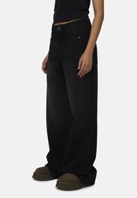 Zwarte wijd uitgesneden jeans van denim, met een hoge taille, zakken en contrasterende stiksels, gecombineerd met bruine grofgebouwde schoenen.