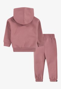 Survêtement en coton rose comprenant un sweat à capuche avec des poignets côtelés et un pantalon assorti à taille élastique avec des chevilles fuselées.