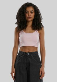 Rosa avkortet tanktopp laget av glatt stoff, med rund hals og brodert logo. Kombinert med høytlivs mørke denimshorts.