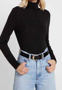 Maglione nero a maniche lunghe con collo alto, in tessuto morbido, abbinato a jeans a vita alta di colore azzurro chiaro, con una cintura nera lucida e fibbia dorata.