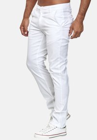 Weiße, schmal geschnittene Baumwollhose mit glatter Textur, normalen Taschen und Reißverschluss, kombiniert mit weißen Sneakers mit roten Akzenten.