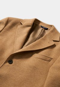 Kamelbrauner Wollblazer mit Reverskragen, einreihiger Knopfleiste und Brusttasche. Glattes Innenfutter sichtbar.