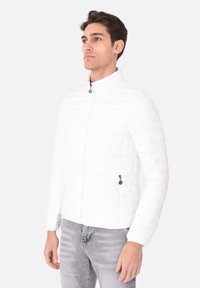 Giacca bianca trapuntata con colletto alto e chiusura con zip. Presenta due tasche laterali con zip e un design slim fit. Tessuto morbido.