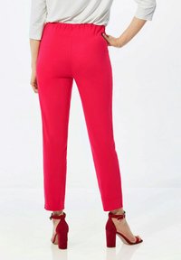 Pantalons slim-fit rose vif avec une taille élastique, présentant un design élégant et une coupe taille cheville, associés à des escarpins rouges.