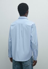 Lichtblauwe overhemd met lange mouwen, een klassieke kraag, met knoopmanchetten, een gladde textuur en een plooidetail op de rug. Draag het met denim.