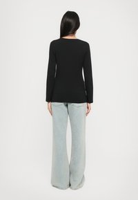 Schwarzes langärmliges Oberteil mit rundem Halsausschnitt, kombiniert mit hellblauen weit geschnittenen Jeans. Der Stoff ist glatt und anliegend.