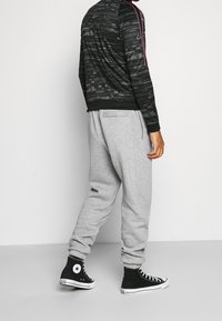 Černá bunda na zip s růžovými akcenty a vzorem, doplněná šedými tepláky. Čistý design, vyrobený z měkké látky, s elastickými manžetami a pasem.