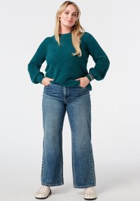 Turquoise gebreide trui met een ronde hals, gecombineerd met hooggetailleerde, wijd uitlopende blauwe jeans en witte slip-on schoenen met studs.