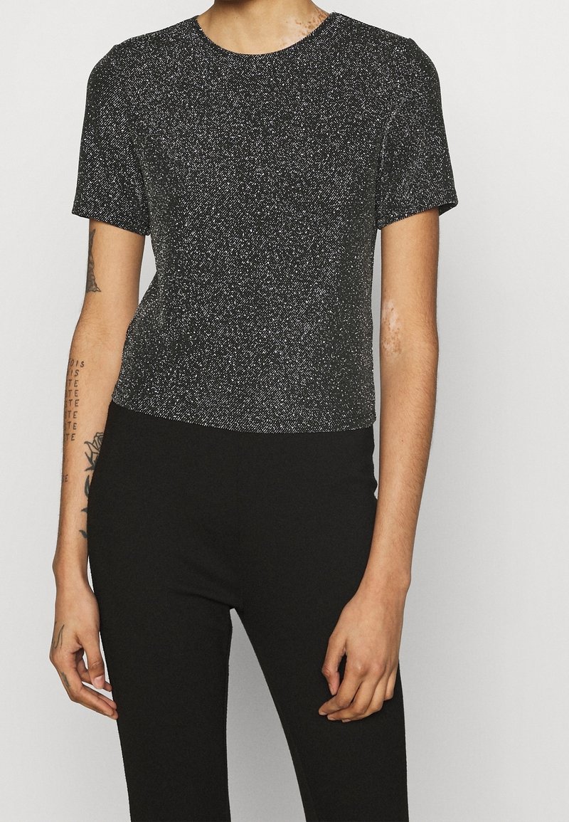 Haut noir à manches courtes avec une texture scintillante, col rond et coupe ajustée. Associé à un pantalon noir taille haute.