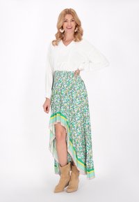 Maglietta bianca a maniche lunghe con scollo a V, abbinata a una gonna alta dietro e bassa davanti con un motivo verde e giallo, e stivali alla caviglia color beige. Presenta un design floreale e righe.