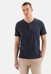 Marineblå bomulds T-shirt med rund halsudskæring, tre-knapslukning og korte ærmer. Fremhæver et lille logo på brystet.