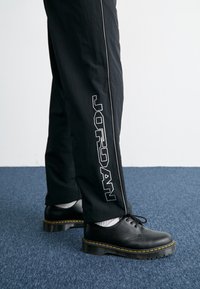 Black casual pants with white piping and "JORDAN" logo on the side, paired with black shoes featuring yellow stitching and thick soles.