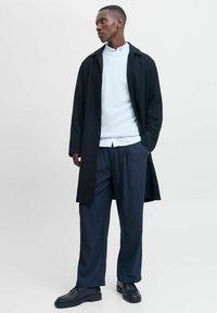 Sort lang frakke over en lyseblå sweater og hvid skjorte; marineblå stribede bukser og sorte sko fuldender looket. Høj kvalitetsstof teksturer.