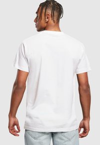 T-shirt en coton blanc à manches courtes et à encolure ronde, avec une texture lisse et une coupe décontractée. Le dos est uni.