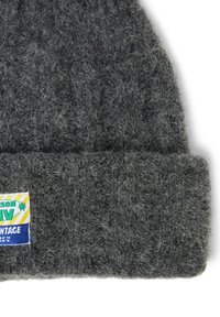 Gray knitted beanie with a textured finish. Features a folded cuff and a colorful label with text and design on one side.