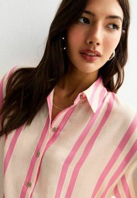 Camisa ligera de botones con rayas verticales en rosa y crema, con cuello y textura suave. El diseño se acentúa con detalles en plata.