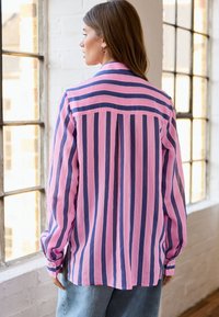 Long-sleeve shirt featuring alternating pink and dark blue vertical stripes, collared design, buttoned cuffs, and a relaxed fit.