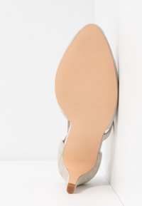 Chaussure à talon haut en daim beige à bout pointu, debout, montrant une semelle lisse marron clair et une petite pointe de talon.