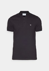 Polo negro de algodón suave con cuello clásico, tapeta de dos botones y pequeño logo bordado en el lado izquierdo del pecho.