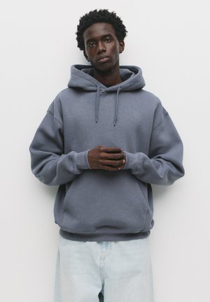 Gray hooded sweatshirt made of soft fabric, featuring a kangaroo pocket and drawstring. Paired with light wash, loose-fitting jeans.