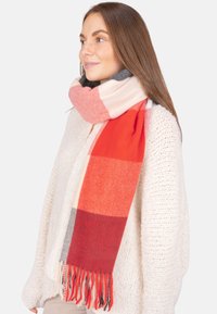 Écharpe à carreaux rouge et rose en tissu doux et tissé. Présente des extrémités à franges et un design en blocs de couleurs avec du crème, du gris et des nuances de rouge.