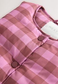 Padded vest in pink and burgundy check pattern, featuring round maroon buttons and a round neckline. Smooth texture, lightweight fabric.
