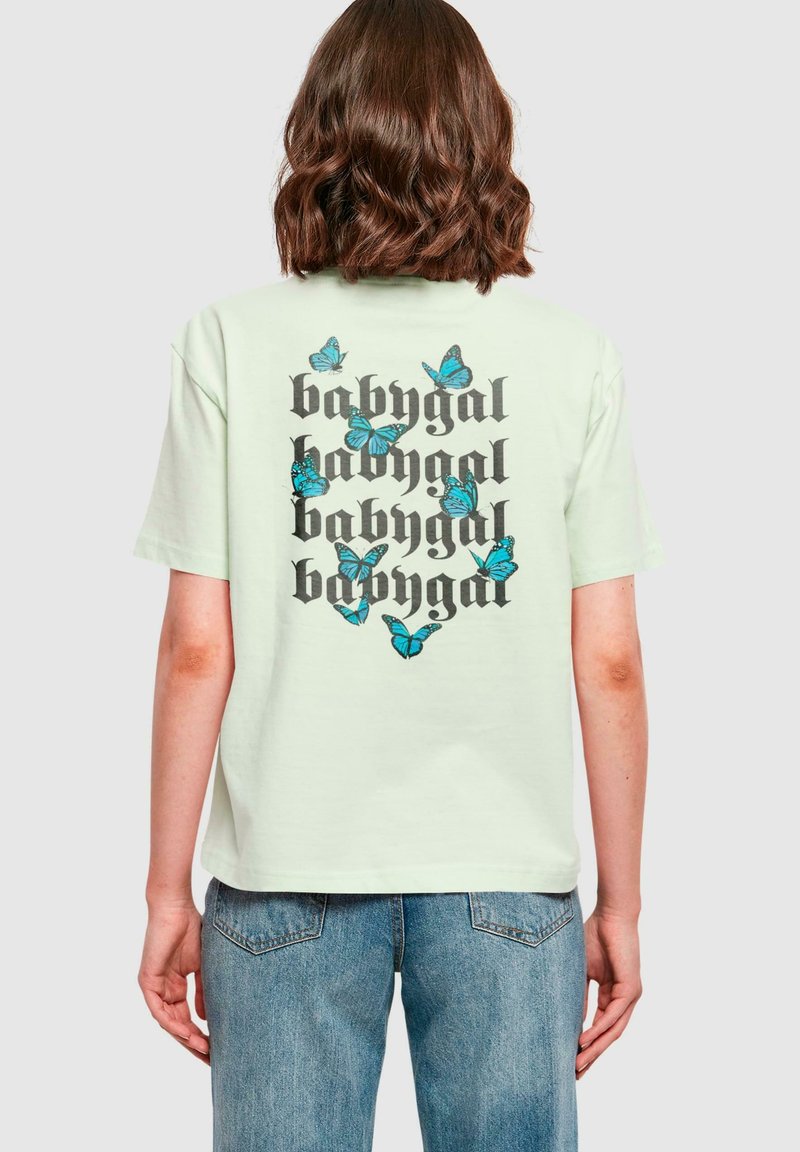 Světle zelené bavlněné tričko se černým nápisem "babygal" a modrými grafikami motýlů na zadní straně. Krátké rukávy a uvolněný střih.