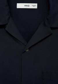 Marineblauwe korte mouw shirt van textuurstof. Kenmerken zijn een open kraag, een enkele knoop en een patchzak aan de voorkant.