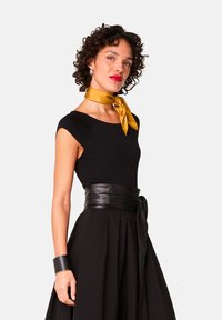 Zwarte aansluitende top met korte mouwen, gecombineerd met een zwarte geplooide rok. Geaccentueerd met een gouden stippen sjaal en een zwarte leren riem.