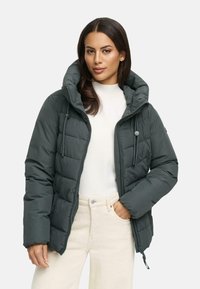 Tumši zaļš pūkainais jaka ar rāvējslēdzēju priekšā, lielu kapuci un quilted rakstu. Viegls materiāls, pieguļoši aproces un divas priekšējās kabatas.