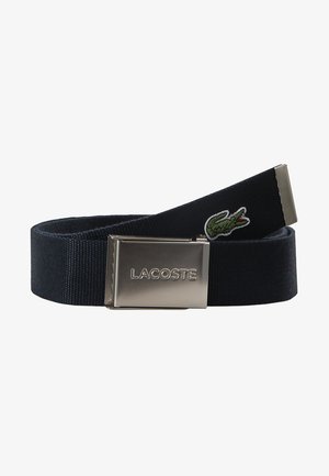 Mornarica tkanina pojas s metalnom kopčom koja sadrži "LACOSTE" logo. Uključuje zeleni izvezeni krokodil. Tekstura površine.