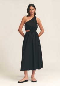 Vestido negro de un solo hombro con cintura fruncida, detalle de corte, falda fluida y tela ligera. Combinado con sandalias nude.