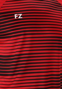 Paita urheiluun punaisilla ja mustilla raidoilla, valmistettu kevyestä kankaasta, jossa on valkoinen "FZ" -logo vasemmassa yläkulmassa. Sileä pinta.