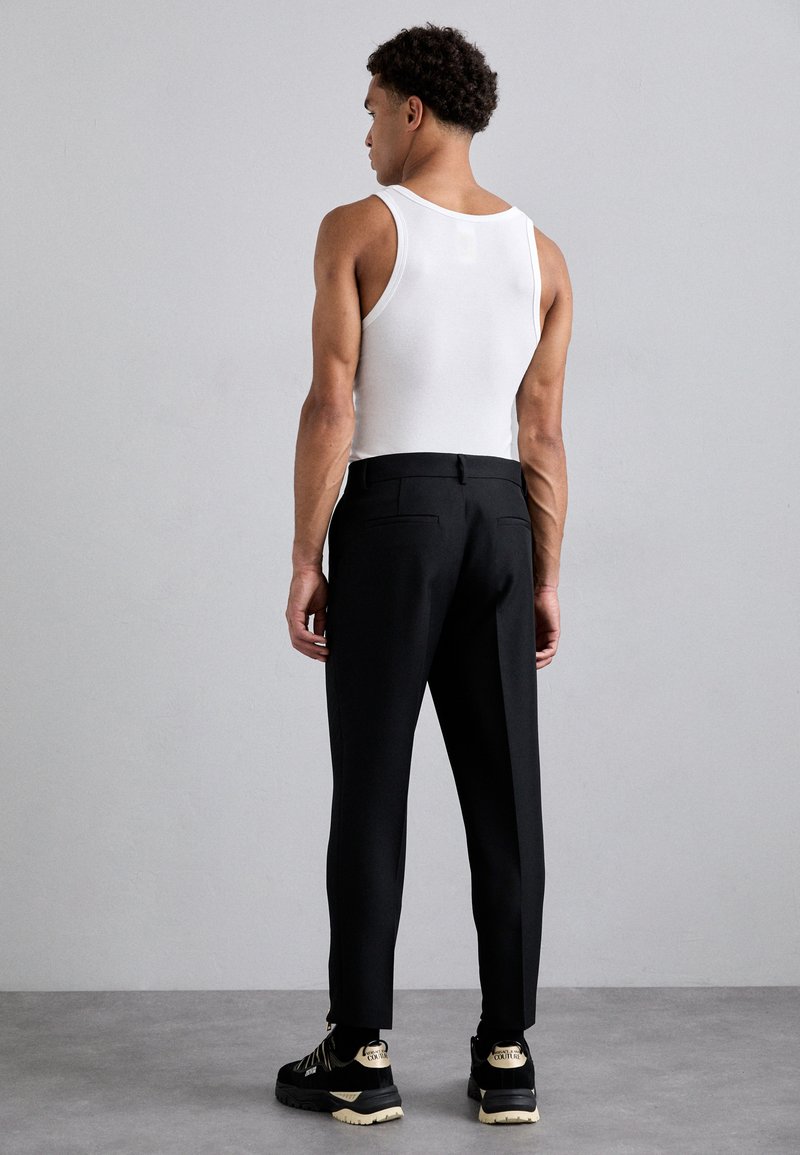 Zwarte op maat gemaakte broek en een witte tanktop, met een aansluitend ontwerp, een gladde textuur en details van achterzakken. Draag met zwarte sneakers.