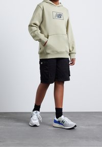 Světlezelená mikina s tmavě šedým logem, v kombinaci s černými cargo šortkami. Bílo-šedé tenisky s modrými a zelenými akcenty.