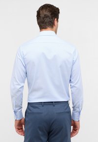 Lichtblauw gestreept overhemd met een standaard kraag, lange mouwen en knopenmanchetten, gecombineerd met donkerblauwe broeken. Gladde stoftextuur.
