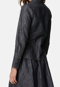 Ciemnoniebieska kurtka dżinsowa o dopasowanym kroju, z kołnierzem, guzikami przy mankietach oraz widocznymi detalami szycia. Tkanina ma fakturowane wykończenie.