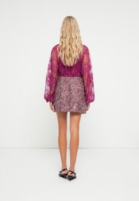 Bluză transparentă, de culoare magenta, cu modele florale și mâneci bufante, combinată cu o fustă mini texturată, cu paiete în nuanțe de argintiu și burgund.