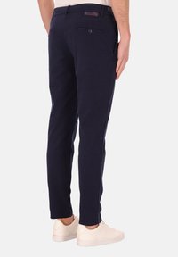 Marineblauwe chino's gemaakt van een katoenmix, met een slim fit, achterzakken en een logo-label op de tailleband, gecombineerd met witte sneakers.