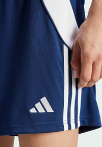 Mornarske atletske kratke hlače s bijelim bočnim prugama, od poliesterskog materijala, s bijelim vezom logoa na rubu i prilagođenim dizajnom.