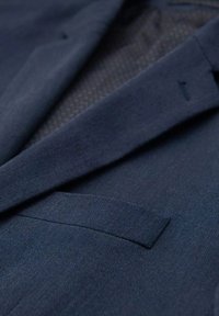 Ciemnoniebieski blazer z teksturą w jodełkę, z klapami typu notch i jedną kieszenią na piersi. Wewnętrzna podszewka odsłania subtelny wzór.