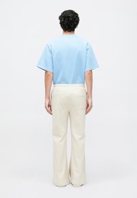 Camisa de manga corta azul claro con escote redondeado, combinada con pantalones anchos color crema que cuentan con un bolsillo trasero. Textura suave, corte relajado.