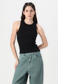 Top nero senza maniche con scollatura rotonda, abbinato a pantaloni larghi di un verde chiaro; materiale morbido con un design semplice.